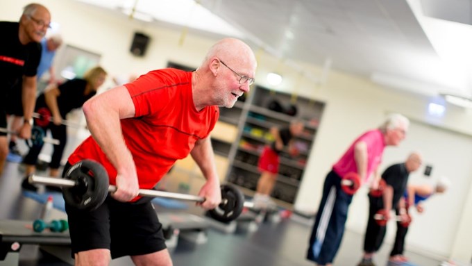 Äldre människor lyfter tyngder i träningslokal