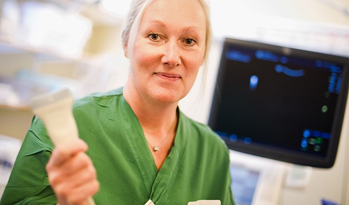 Kvinna klädd i vårdkläder står framför ultraljudsapparat