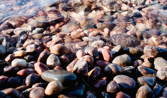 En stor mängd mindre stenar på en strand med vatten rullande in över sig.