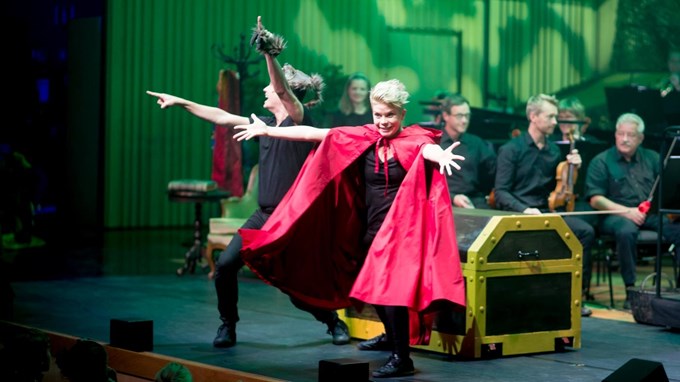 kvinna i röd kappa och man i svarta kläder dansar på en scen. 