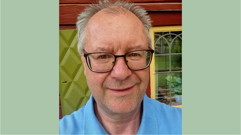 Dennis ler stort, har glasögon och kort grått hår.