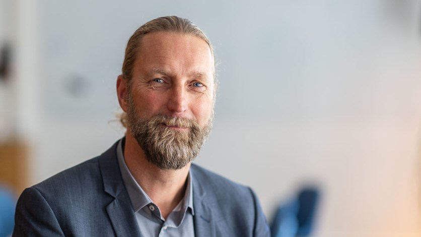 Harald som syns på bilden har uppsatt brunt hår och helskägg. Han är klädd i kavaj och ler mot kameran.