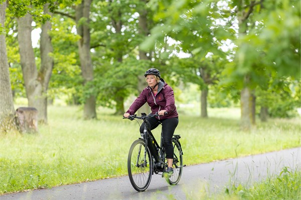 Malin Hagelin cyklar på en cykelbana i en park med gröna träd. 