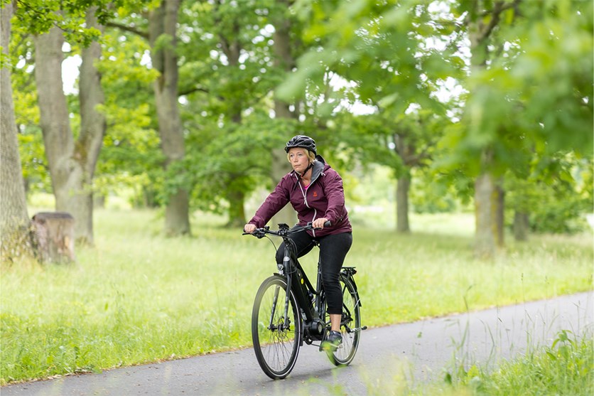 Malin Hagelin cyklar på en cykelbana i en park med gröna träd. 
