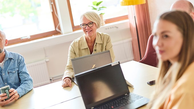 Leende personer som sitter runt ett konferensbord med datorer framför sig.