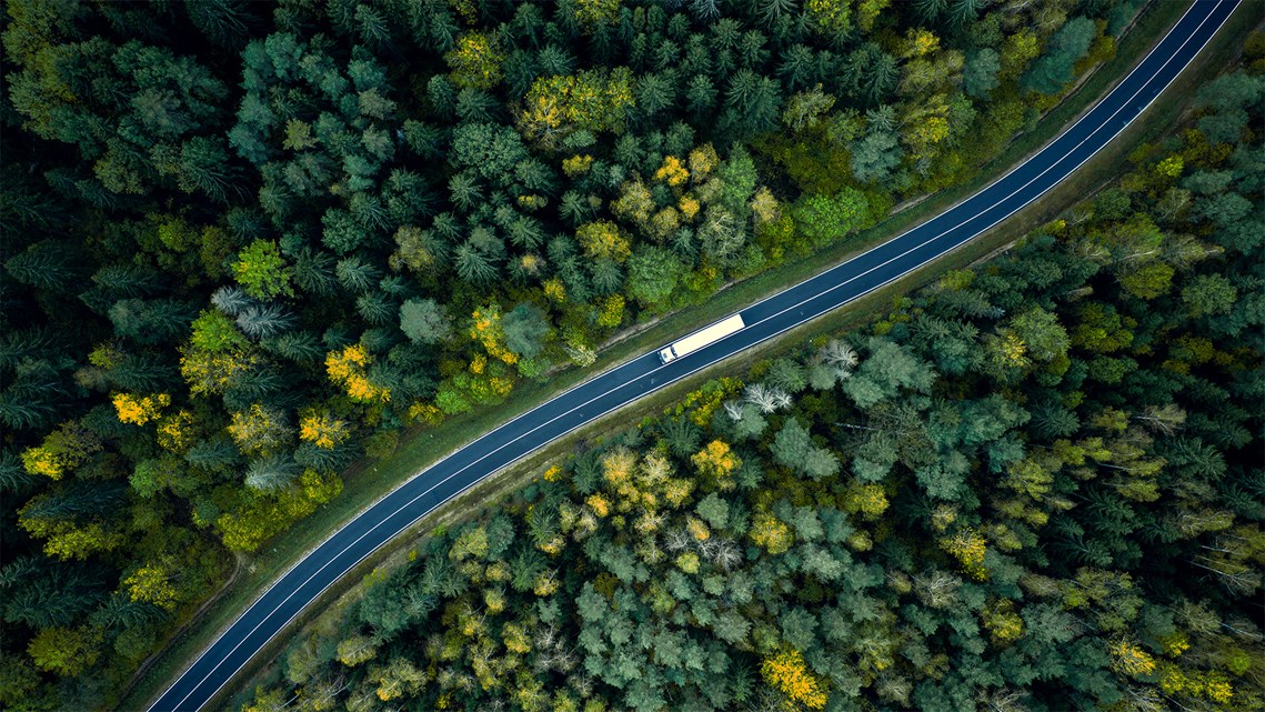 Tung transport på väg bland skog, vy ovanifrån. 