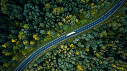 Tung transport på väg bland skog, vy ovanifrån.