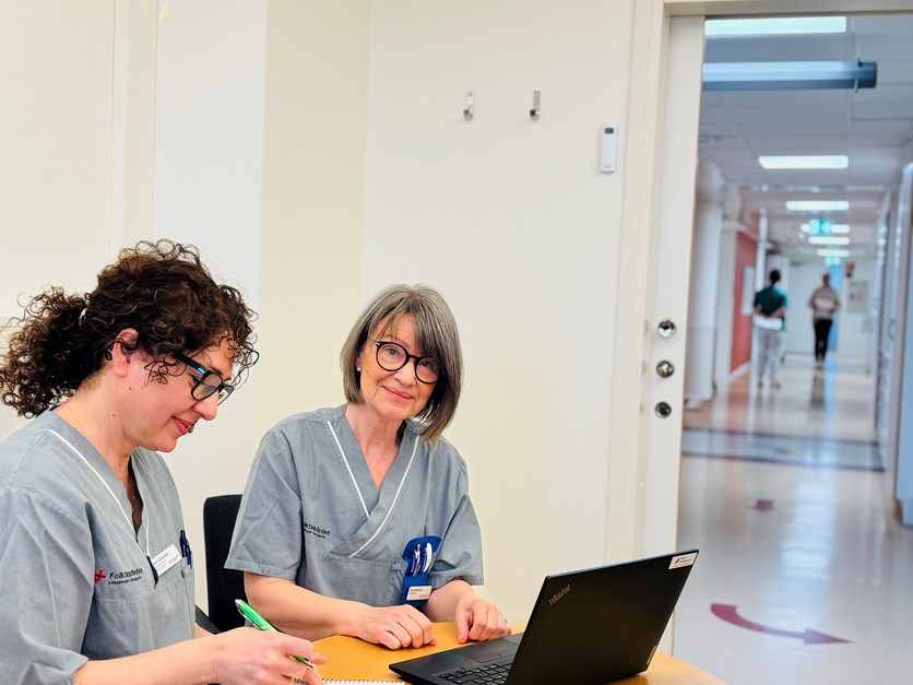 Eva Johansson sitter och arbetar tillsammans med sin chef Maria Kassapidou, i bakgrunden pågår klinikens vardagliga arbete.