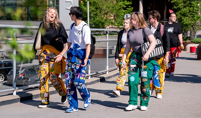 Sex studenter i färgglada overaller går utomhus och skrattar.