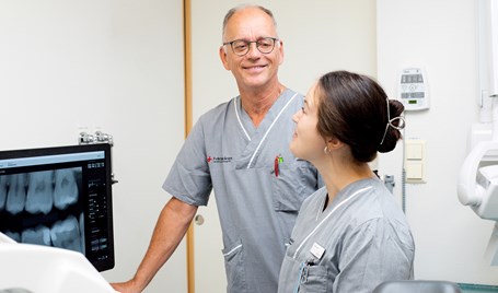 En man och kvinna  tittar på varandra. De står i ett behandlingsrum och är klinikklädda. 