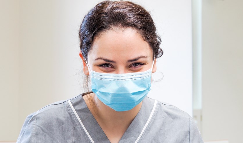 En kvinna i munskydd som tittar in i kameran.