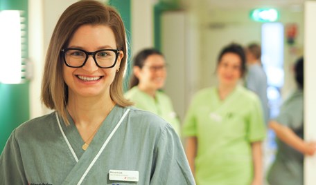 En kvinnlig ledare står framför sina medarbetare i en klinisk miljö.