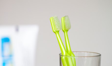 Två gröna tandborstar står i ett dricksglas.