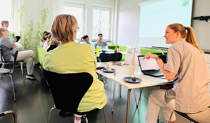 Klinikchefen pratar inför medarbetarna i ett lunchrum.