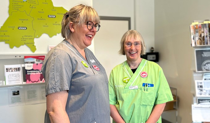 Två kvinnor i klinikkläder står inne på ett kontor och skrattar. 