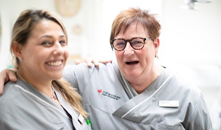 Två kvinnor i klinikkläder håller om varandra och skrattar mot kameran