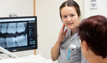 En tandhygienist i samtal med en patient, i bakgrunden en röntgenbild.