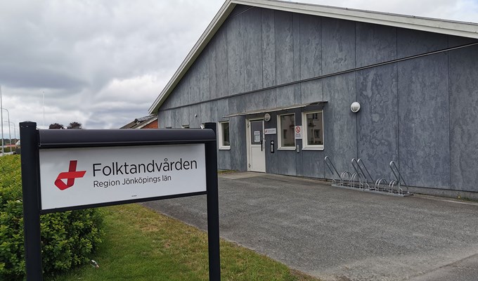 Smålandsstenar Folktandvård entré. En mörkgrå modern byggnad med gräsmatta och buskar framför.