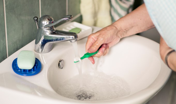 En äldre person som håller en tandborste under rinnande vatten.