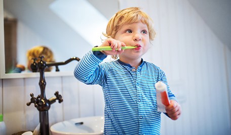 En liten kille suger på en tandborste och håller i en tandkräm.