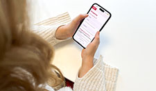 En kvinna håller i en telefon och för att logga in i 1177 och av- eller omboka sin tid hos Folktandvården.