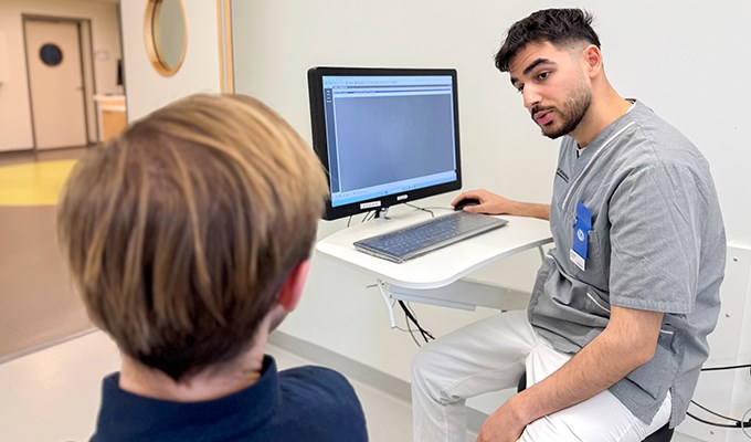 En manlig tandläkare sitter och pratar med en patient. Patienten sitter i en behandlingsstol.