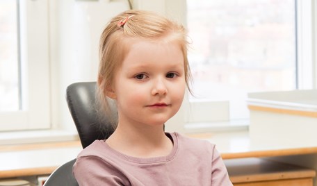 Ett barn sitter i en behandlingsstol och kollar in i kameran.