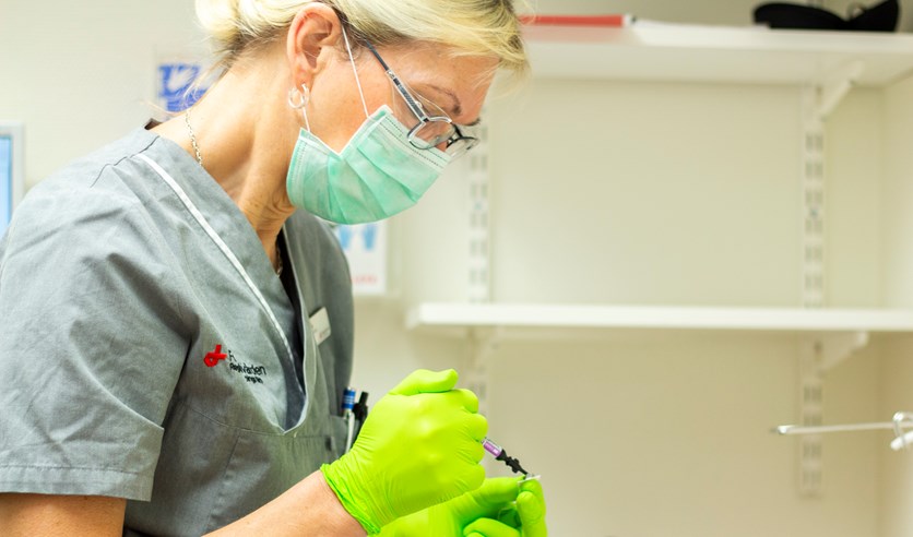 En kvinna sitter med munskydd och plasthandskar jobbar.