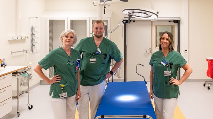 Tre personer i gröna sjukvårdskläder står i ett mottagningsrum på akutmottagning. 