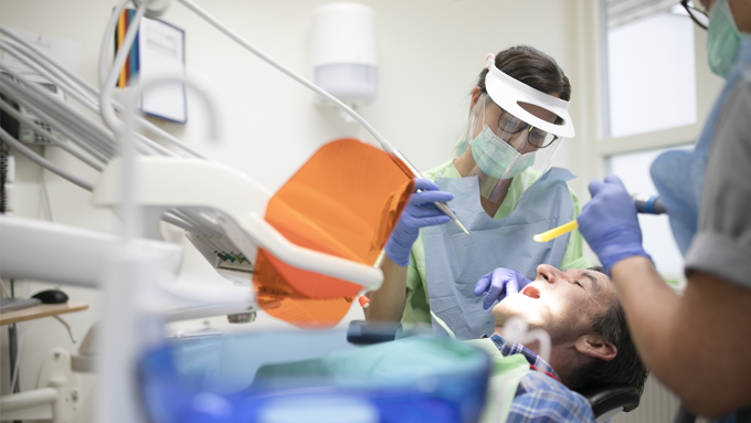 Två tandvårdare som undersöker en patient som ligger ner och gapar.