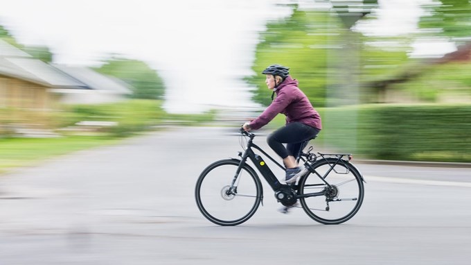 En kvinna med hjälm på huvudet cyklar i hög fart