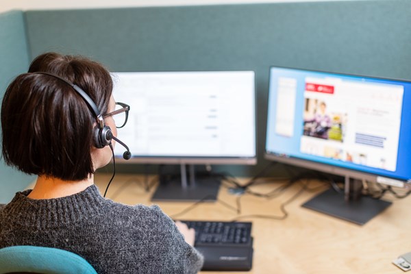 Kvinna med headset sitter framför två datorskärmar.