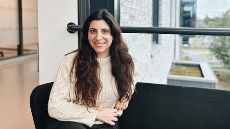 En person sitter i en soffa och ler mot kameran.