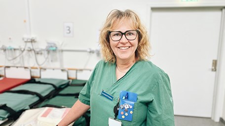 Person ler mot kameran. Hon jobbar på akuten och är klädd i arbetskläder. 
