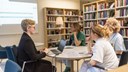 En pågående handledning i informationssökning där en bibliotekarie hjälper tre studenter, de sitter runt ett bord inne på biblioteket. 