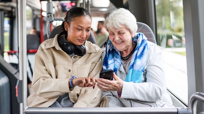 En ung kvinna och en äldre dam sitter bredvid varandra på bussen. 
