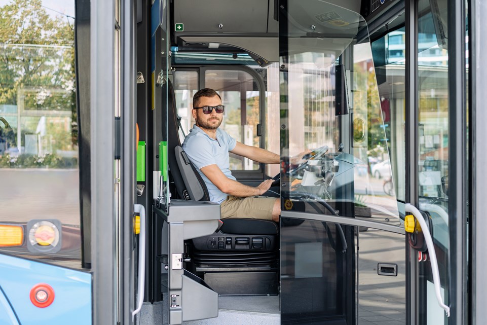 Busschaufför sitter i en buss och tittar ut genom den öppna dörren. 