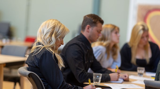 Ett grupparbete pågår i ett klassrum med både kvinnor och män. De sitter vid ett bord och antecknar. 