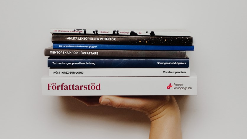 En hand som håller upp en trave med böcker. 