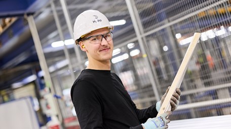 Man i hjälm, handskar och arbetsglasögon som befinner sig i en industrilokal. 