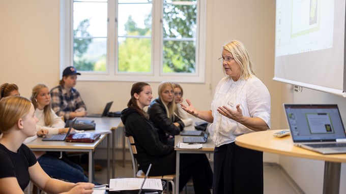 En kvinnlig lärare står framför en skolklass i ett klassrum. 