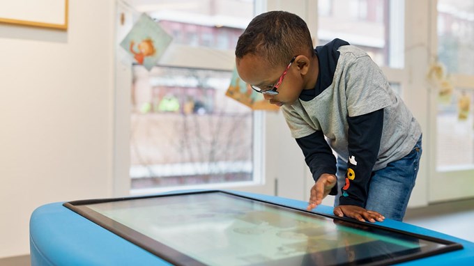 Ett barn står och tittar ner på en stor digital skärm. 