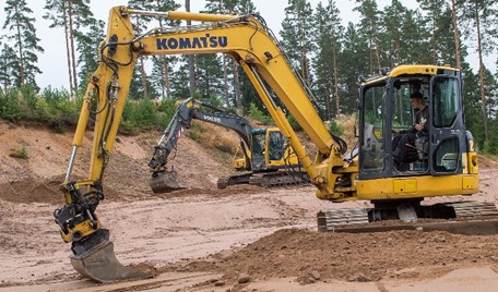 Gula grävmaskiner körd på en grusplan.