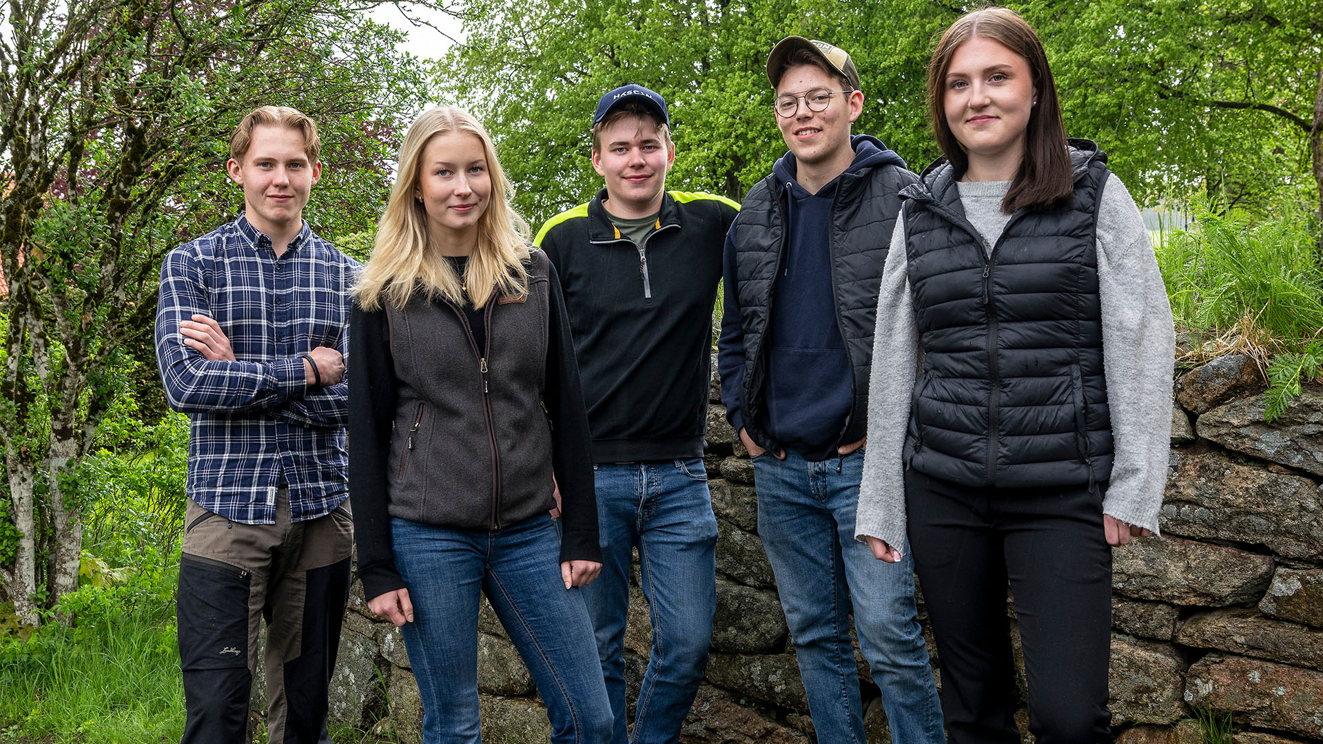 Flera elever står framför en stenmur i grönskan.