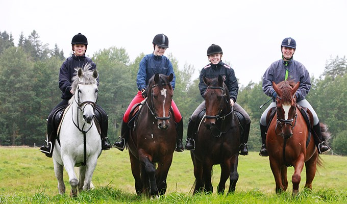 Fyra kvinnliga ryttare till häst ute på ett grönt fält.