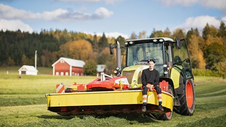 En elev sitter på en traktor på ett fält.