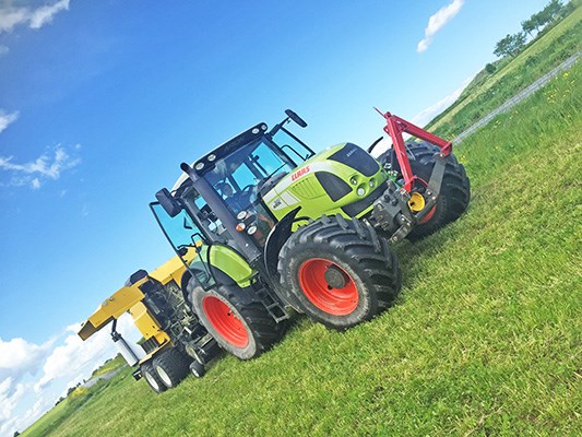 Grön traktor med balpress som körs ute på fältet.