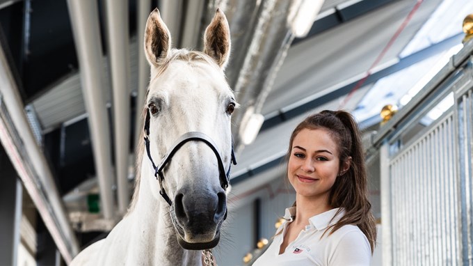 En tjej står tillsammans med en vit häst och ler mot kameran.