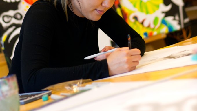 Person i svart tröja tecknar med penna på ett papper
