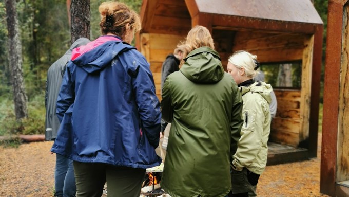 Människor står samlade i ring runt öppen eld i naturen.